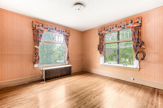 spare room featuring a textured ceiling, plenty of natural light, radiator heating unit, and light wood-type flooring