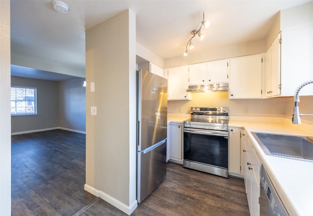 kitchen with dark wood finished floors, appliances with stainless steel finishes, a sink, under cabinet range hood, and baseboards