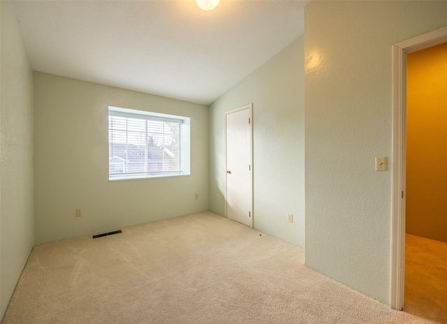 carpeted spare room featuring vaulted ceiling, a textured wall, and visible vents