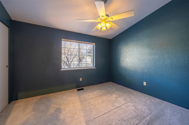 carpeted spare room with ceiling fan, visible vents, vaulted ceiling, and a textured wall