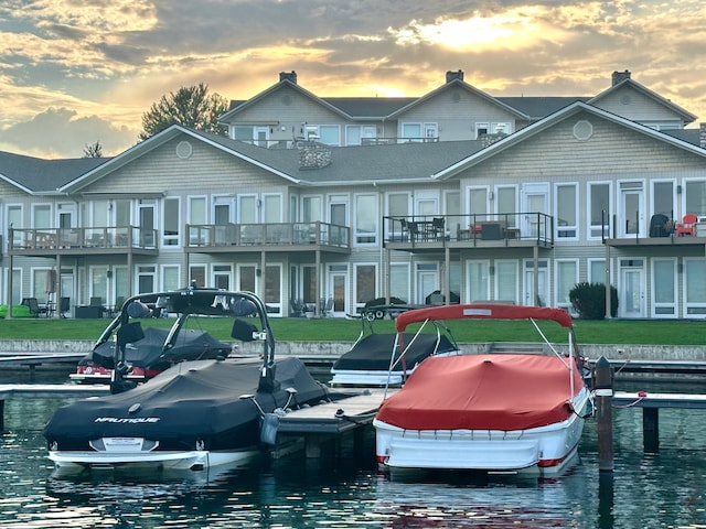 dock area featuring a water view, a balcony, and a lawn