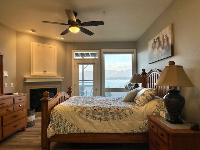 bedroom with a fireplace, access to outside, light hardwood / wood-style floors, and ceiling fan