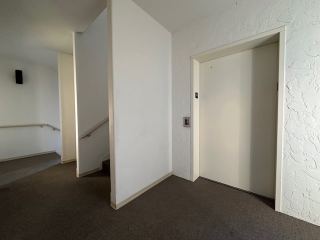 hallway with elevator and dark carpet