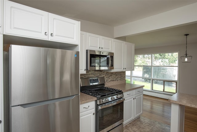 kitchen featuring a baseboard heating unit, white cabinets, tasteful backsplash, hanging light fixtures, and stainless steel appliances