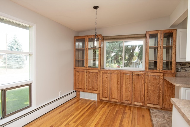 unfurnished dining area featuring a baseboard heating unit, plenty of natural light, light wood finished floors, and visible vents