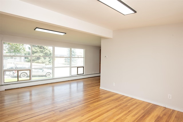 spare room featuring plenty of natural light, baseboards, a baseboard radiator, and light wood-type flooring