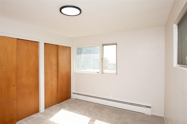 unfurnished bedroom featuring carpet floors, a baseboard heating unit, and two closets