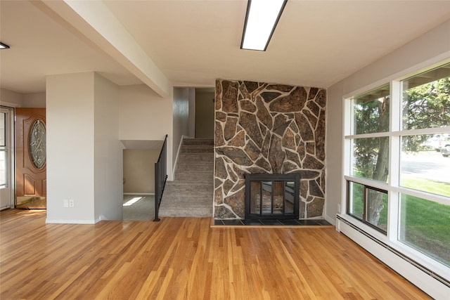 unfurnished living room featuring a stone fireplace, stairs, baseboards, wood finished floors, and a baseboard heating unit
