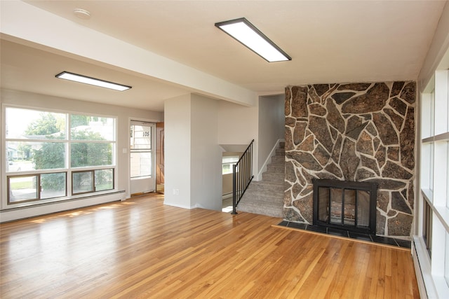 unfurnished living room with a stone fireplace, baseboards, wood finished floors, a baseboard radiator, and a baseboard heating unit