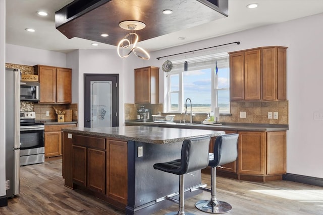 kitchen with wood-type flooring, appliances with stainless steel finishes, tasteful backsplash, and a kitchen island