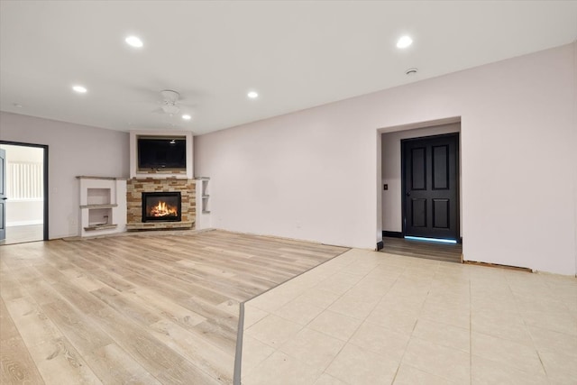 unfurnished living room featuring light hardwood / wood-style floors, ceiling fan, and a stone fireplace