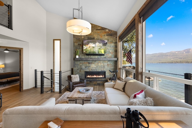 living room with a water and mountain view, a stone fireplace, high vaulted ceiling, and hardwood / wood-style flooring