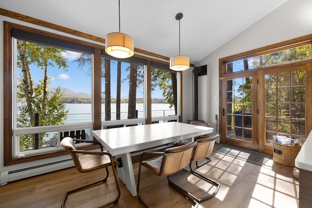 dining space featuring light hardwood / wood-style flooring, a wood stove, baseboard heating, a water view, and lofted ceiling