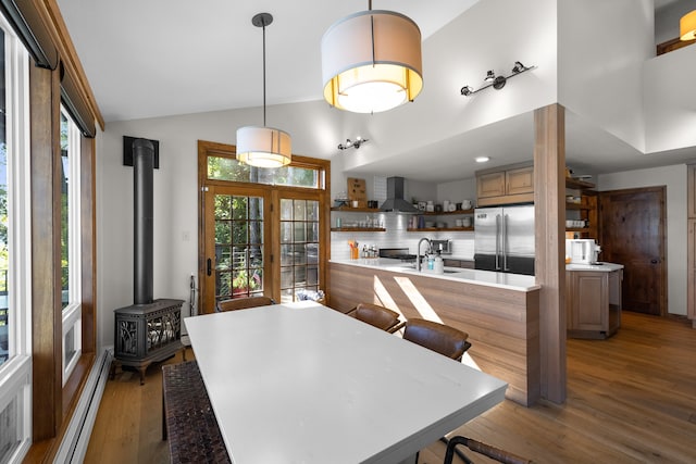 interior space featuring built in fridge, wall chimney exhaust hood, wood-type flooring, and a wood stove