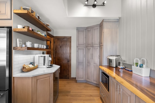 kitchen with stainless steel refrigerator, wooden walls, light hardwood / wood-style flooring, wooden counters, and black microwave