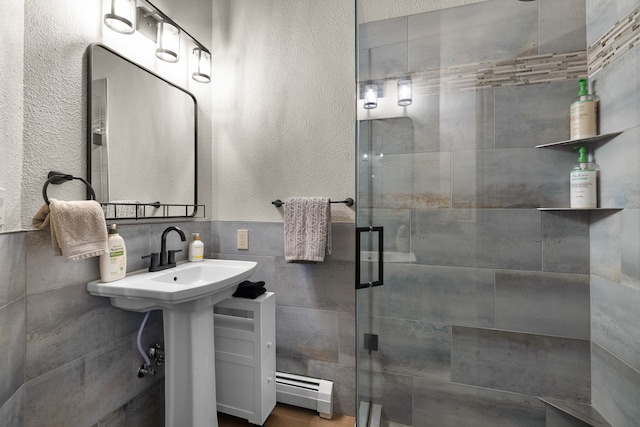 bathroom featuring a shower with shower door, baseboard heating, and tile walls