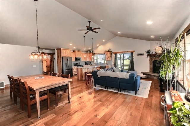 dining space with ceiling fan with notable chandelier, a fireplace, wood-type flooring, and vaulted ceiling