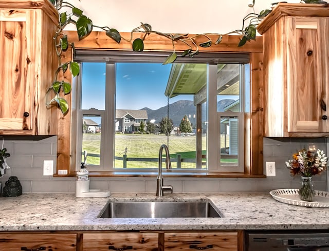 kitchen featuring dishwasher, a mountain view, sink, light stone countertops, and decorative backsplash