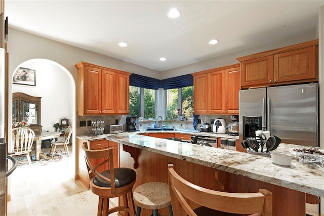 kitchen featuring light stone counters, a breakfast bar area, a sink, stainless steel refrigerator with ice dispenser, and tasteful backsplash