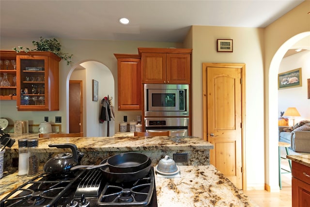 kitchen featuring stainless steel appliances, arched walkways, glass insert cabinets, and light stone counters