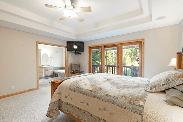 carpeted bedroom featuring ceiling fan, ensuite bathroom, baseboards, access to exterior, and a tray ceiling