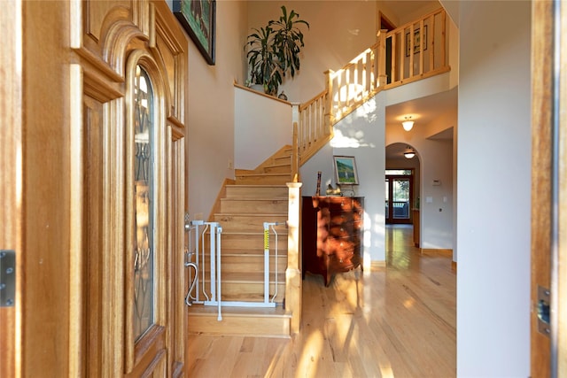 foyer entrance with stairs, a high ceiling, arched walkways, and wood finished floors