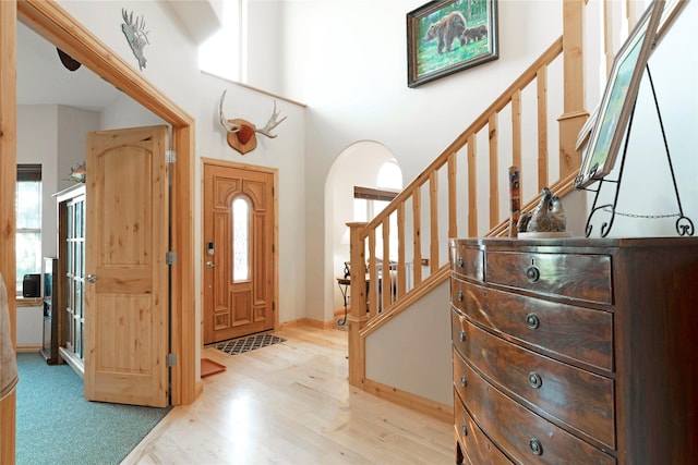 entrance foyer with arched walkways, stairway, light wood-type flooring, and a wealth of natural light