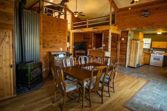 dining area with wood walls, ceiling fan, a wood stove, and dark hardwood / wood-style floors