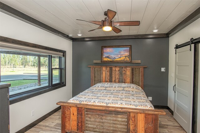 bedroom featuring ceiling fan, a barn door, light wood-type flooring, and wood ceiling