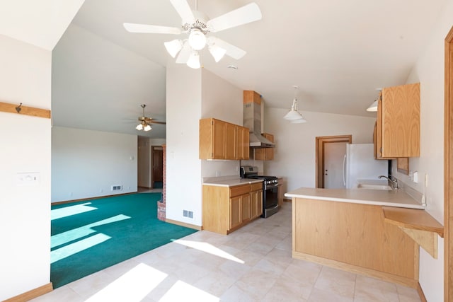 kitchen with vaulted ceiling, kitchen peninsula, stainless steel gas range oven, wall chimney exhaust hood, and ceiling fan