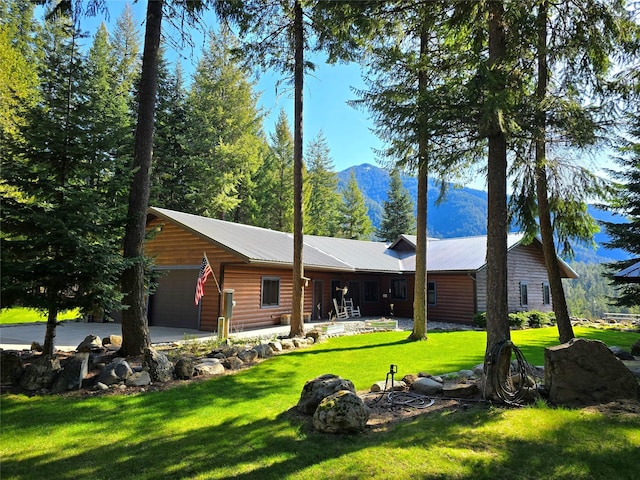 rear view of property featuring a lawn, faux log siding, a mountain view, and a garage