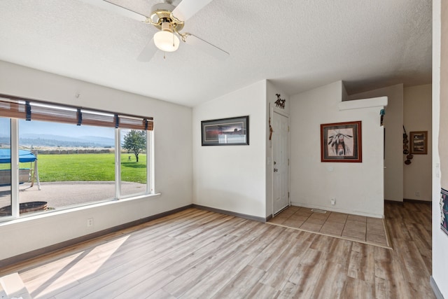 spare room with lofted ceiling, a textured ceiling, ceiling fan, and light hardwood / wood-style floors