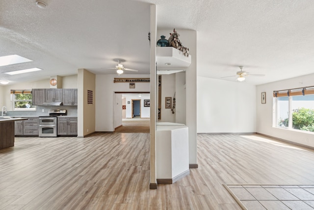 unfurnished living room with lofted ceiling with skylight, light wood-type flooring, sink, ceiling fan, and a textured ceiling