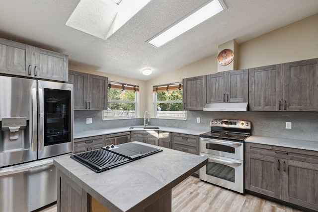 kitchen featuring backsplash, stainless steel appliances, sink, vaulted ceiling with skylight, and a kitchen island