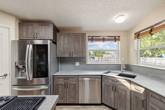 kitchen with appliances with stainless steel finishes, light hardwood / wood-style floors, sink, tasteful backsplash, and a textured ceiling