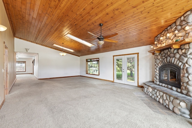 unfurnished living room with vaulted ceiling with skylight, ceiling fan, a stone fireplace, wood ceiling, and light colored carpet