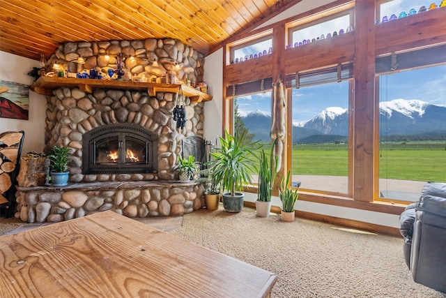 carpeted living room with a mountain view, vaulted ceiling, wooden ceiling, and a stone fireplace