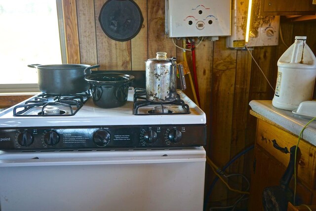 details with white range with gas stovetop, water heater, and wood walls