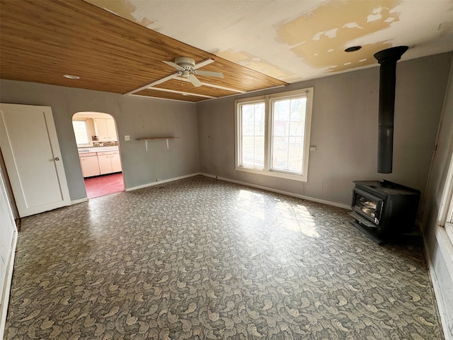 unfurnished living room featuring wooden ceiling, ceiling fan, and a wood stove