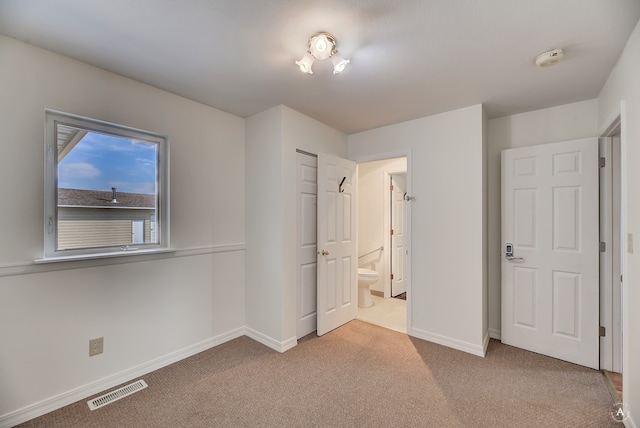 unfurnished bedroom with ensuite bath, a closet, and carpet flooring