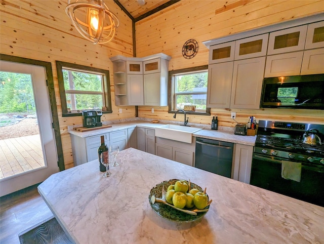 kitchen with pendant lighting, wood walls, vaulted ceiling, sink, and appliances with stainless steel finishes