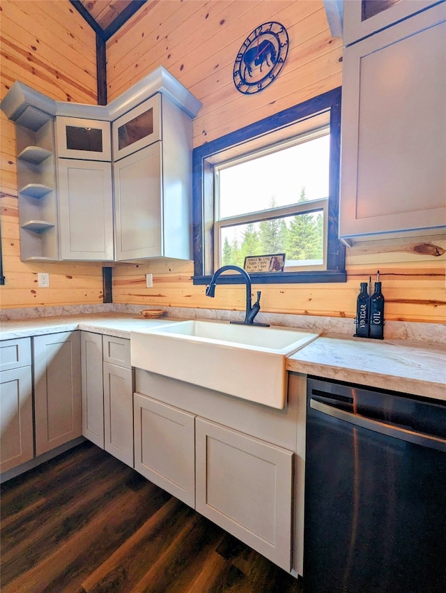 kitchen with stainless steel dishwasher, sink, wooden walls, and dark wood-type flooring