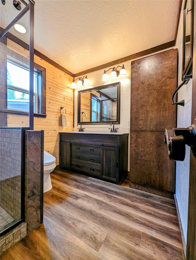 bathroom featuring toilet, wood-type flooring, vanity, wood walls, and a textured ceiling