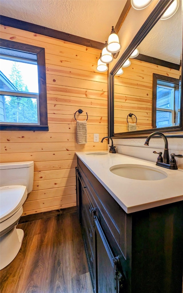 bathroom with a textured ceiling, vanity, wood walls, hardwood / wood-style floors, and toilet