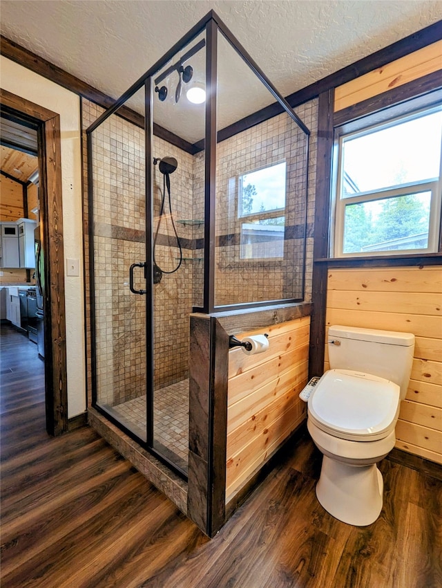 bathroom with toilet, hardwood / wood-style floors, a shower with door, a textured ceiling, and wood walls