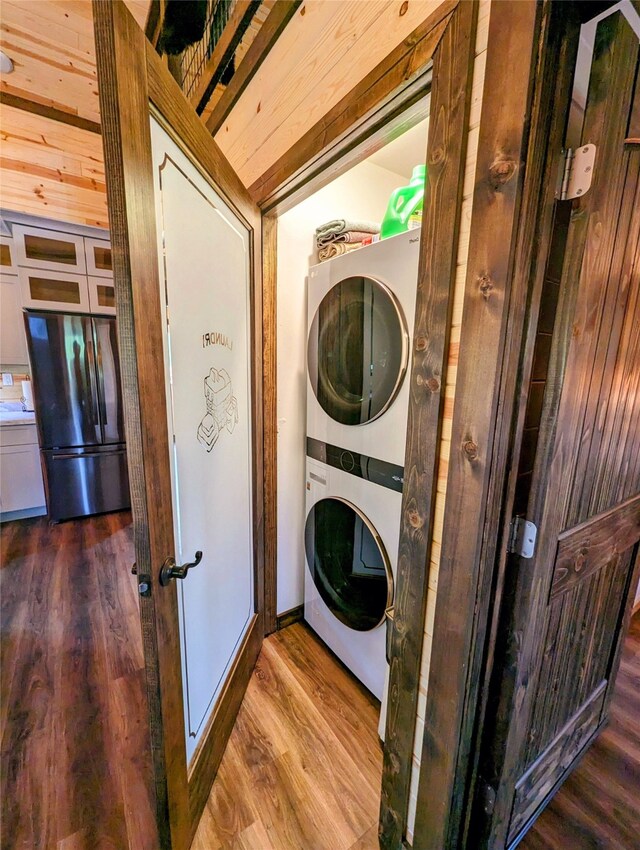 laundry room with dark wood-type flooring, stacked washer and dryer, and wooden walls