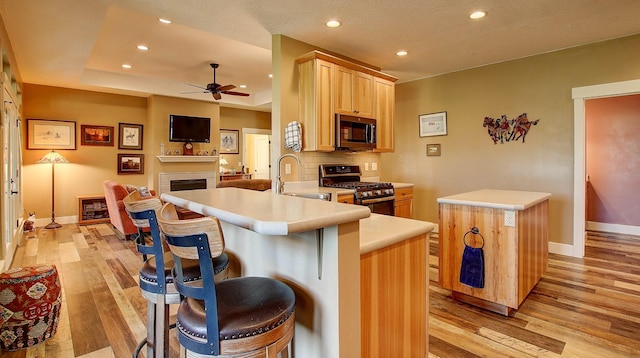 kitchen with appliances with stainless steel finishes, light brown cabinetry, sink, kitchen peninsula, and light hardwood / wood-style flooring