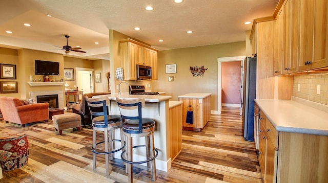 kitchen with light hardwood / wood-style flooring, a breakfast bar, appliances with stainless steel finishes, tasteful backsplash, and kitchen peninsula