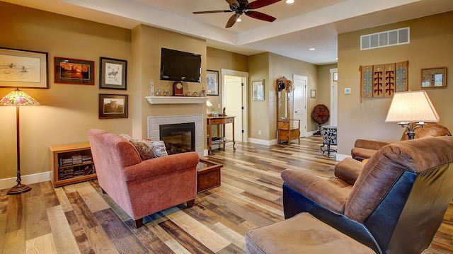 living room featuring ceiling fan, a tile fireplace, and light wood-type flooring