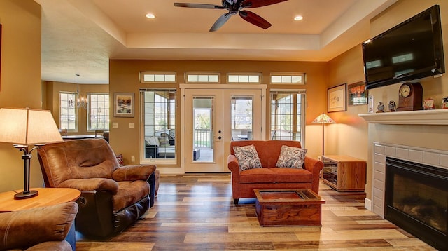 living room featuring a tile fireplace, wood-type flooring, ceiling fan with notable chandelier, and french doors